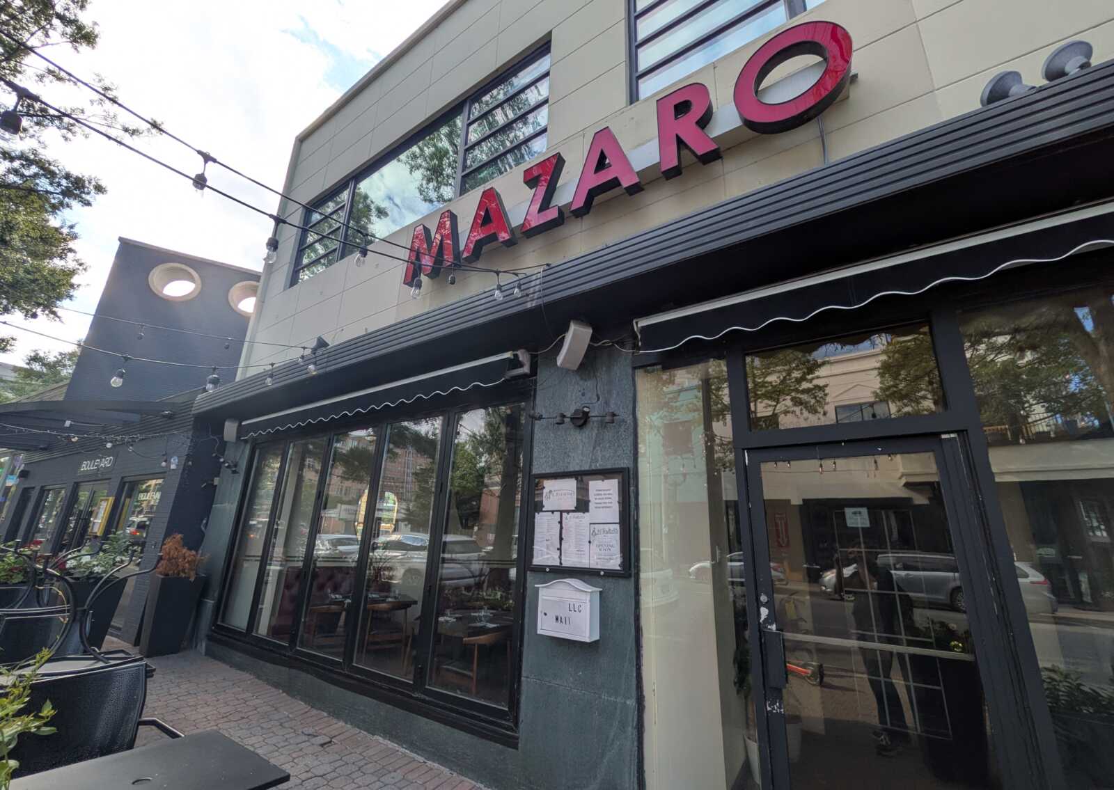 Exterior view of a modern storefront with a red MAZARO sign, string lights, and large glass windows.
