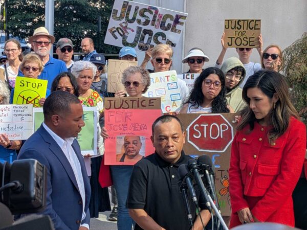 Crowd of protesters holding signs reading Justice for José and Stop, gathered at a street demonstration behind a speaker podium.
