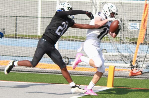 Two football players sprint near the sideline; a white-jersey runner holds the ball while a black-jersey defender reaches in to tackle him.
