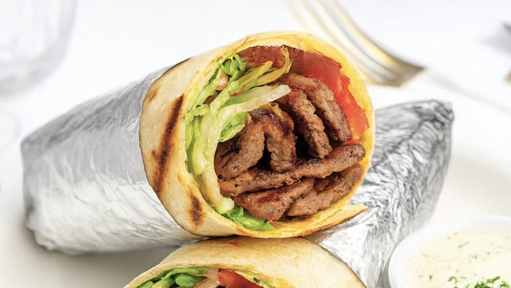 Beef gyro wrap sliced open showing grilled meat, lettuce, and tomato in a warm flatbread