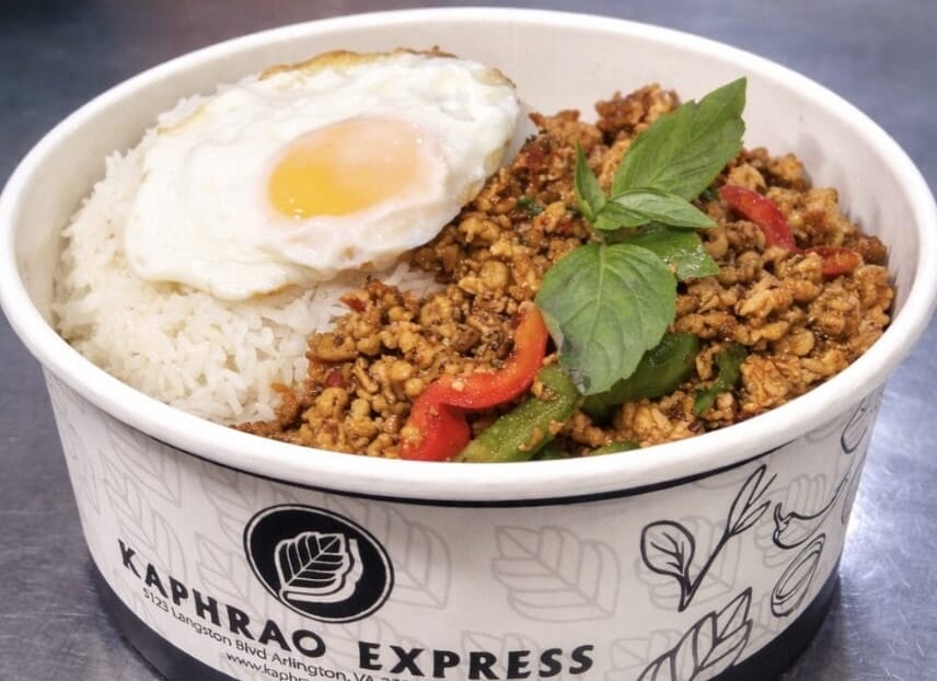 Rice bowl with a sunny-side-up egg, stir-fried minced chicken and peppers, garnished with basil in a takeout cup labeled Kaphrao Express