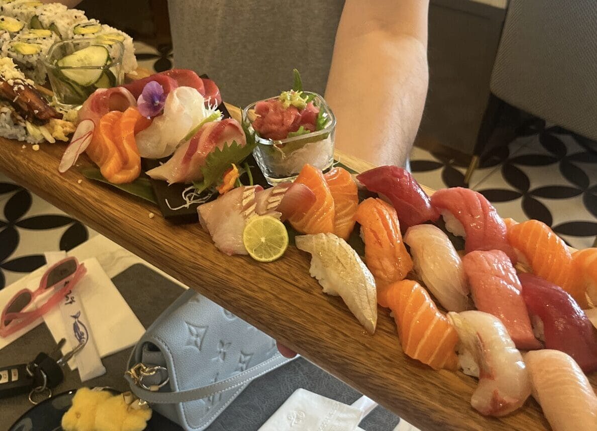 Assorted sushi and sashimi platter on a wooden board with lime wedge and garnishes.