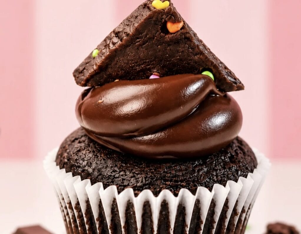 Chocolate cupcake with glossy chocolate frosting, topped by a triangular chocolate shard with colorful sprinkles.