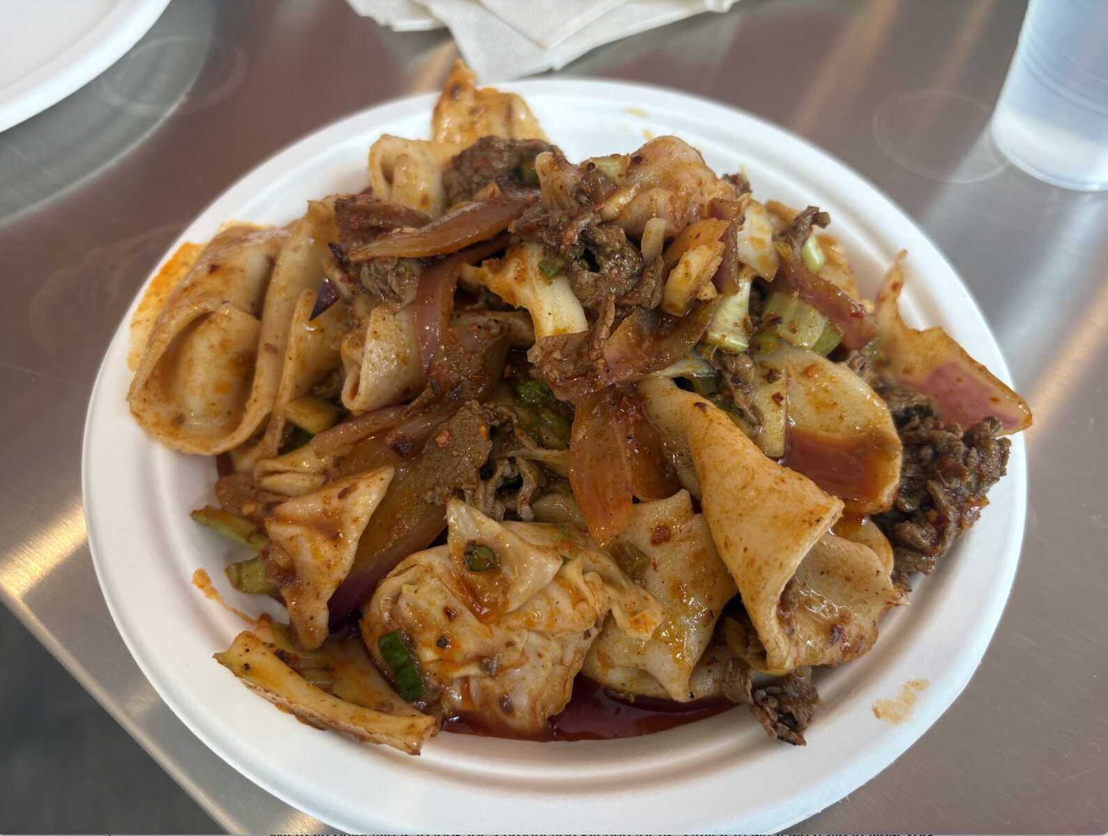 Spicy stir-fried flat noodles with beef, onions, and peppers on a white plate.