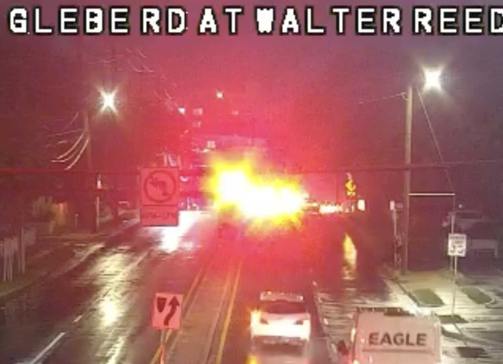 Nighttime street scene with flashing red and yellow emergency lights and roadwork barriers blocking lanes.
