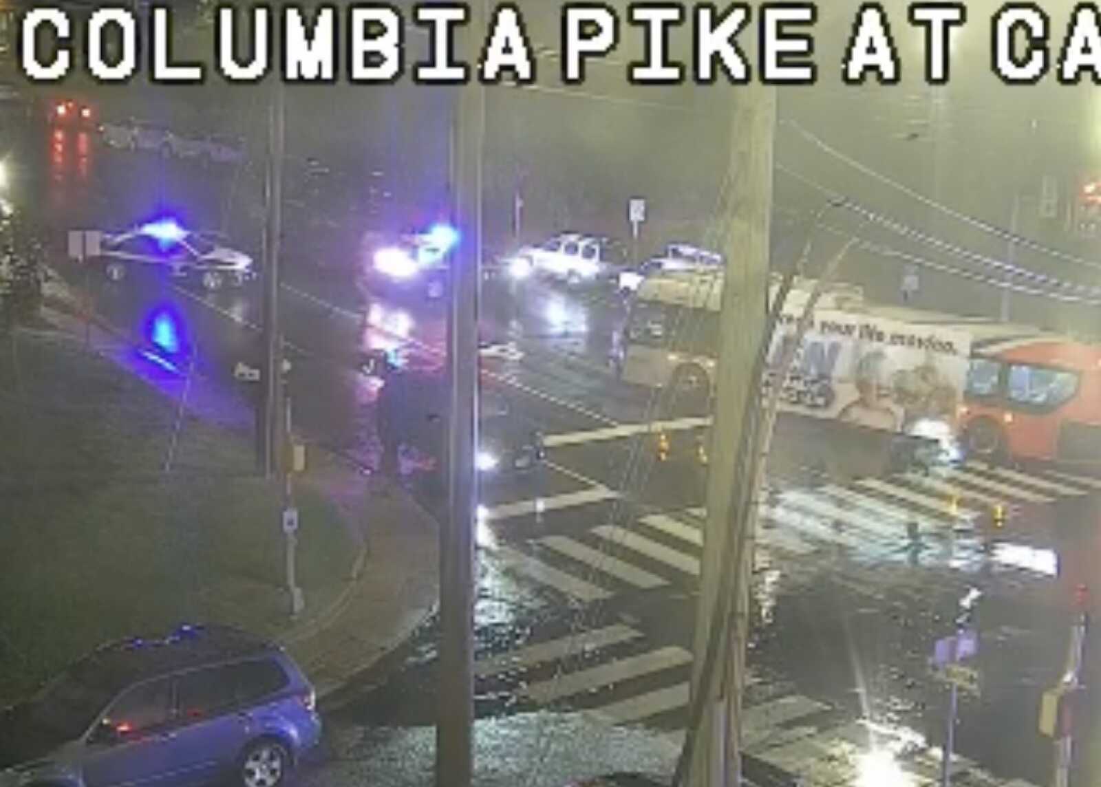 Emergency response at a nighttime intersection with police cars flashing blue lights and an ambulance on Columbia Pike (wet street).