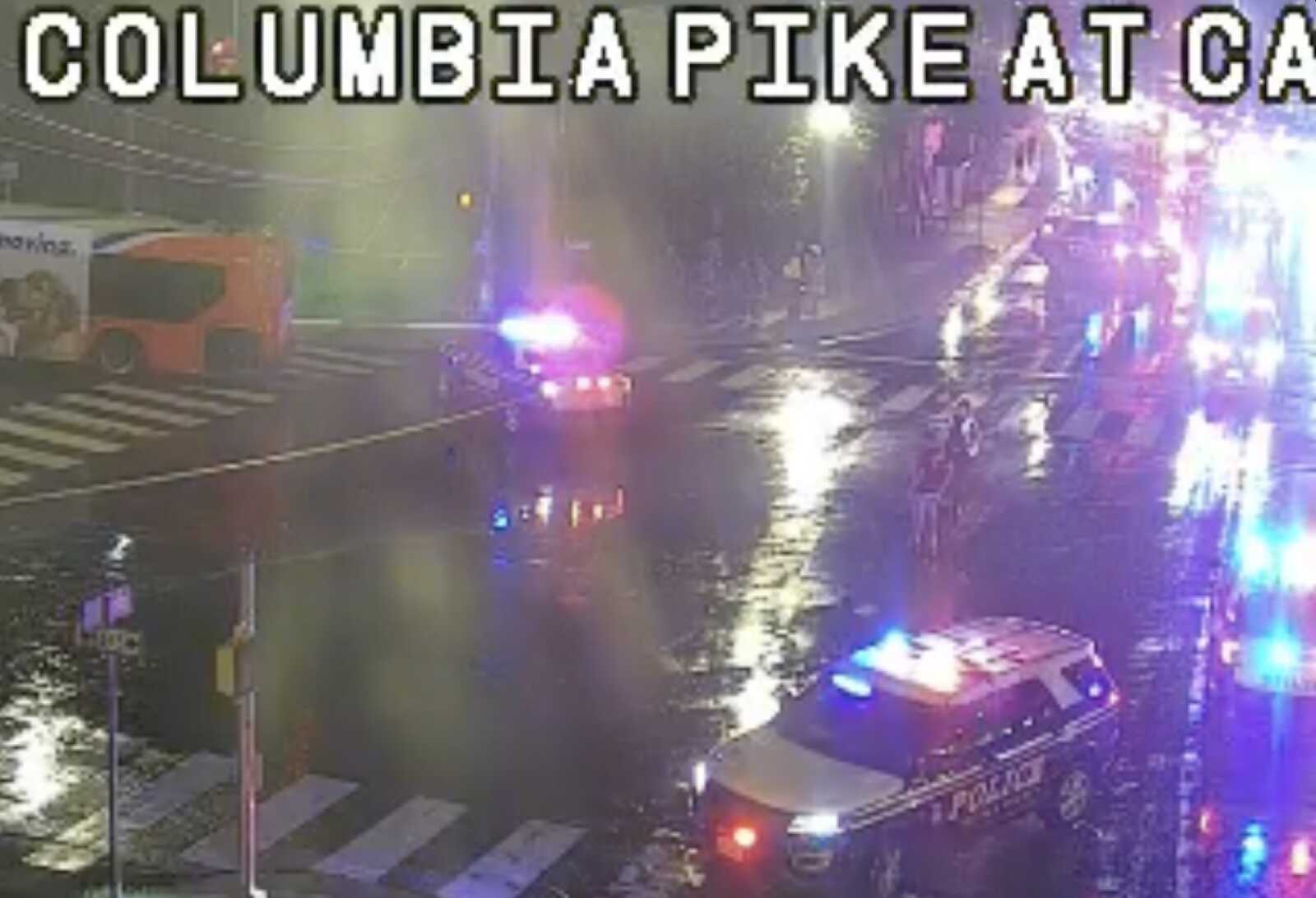 Nighttime street scene with police and ambulance vehicles and flashing blue and red lights on a wet road, Columbia Pike area.