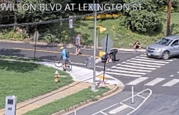 Crosswalk at Wilson Blvd and Lexington St: a cyclist on a blue bike rides by while a gray car waits at the intersection.
