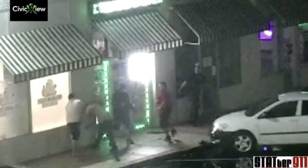 Nighttime street scene outside a storefront with striped awnings and a group of people walking past a bright doorway with green neon lights.