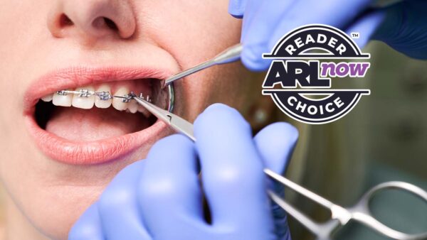 Dentist wearing blue gloves adjusting a patient's braces with dental tools in the mouth.