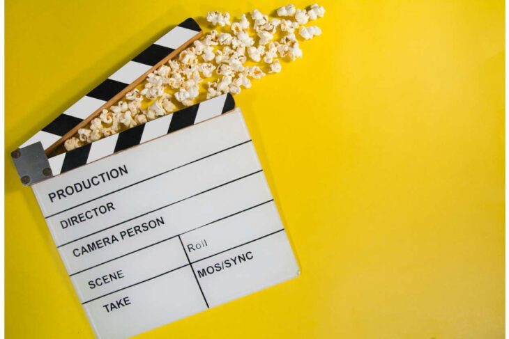 White film clapperboard with popcorn spilling along a yellow background, signaling movie production.