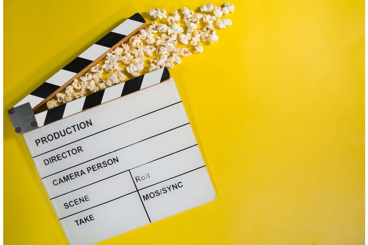 White film clapperboard with popcorn spilling along a yellow background, signaling movie production.
