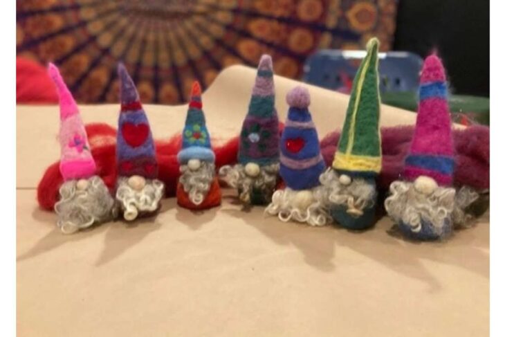 Row of colorful felt gnome figurines with tall hats and fluffy beards on a table surface, arranged in a line.