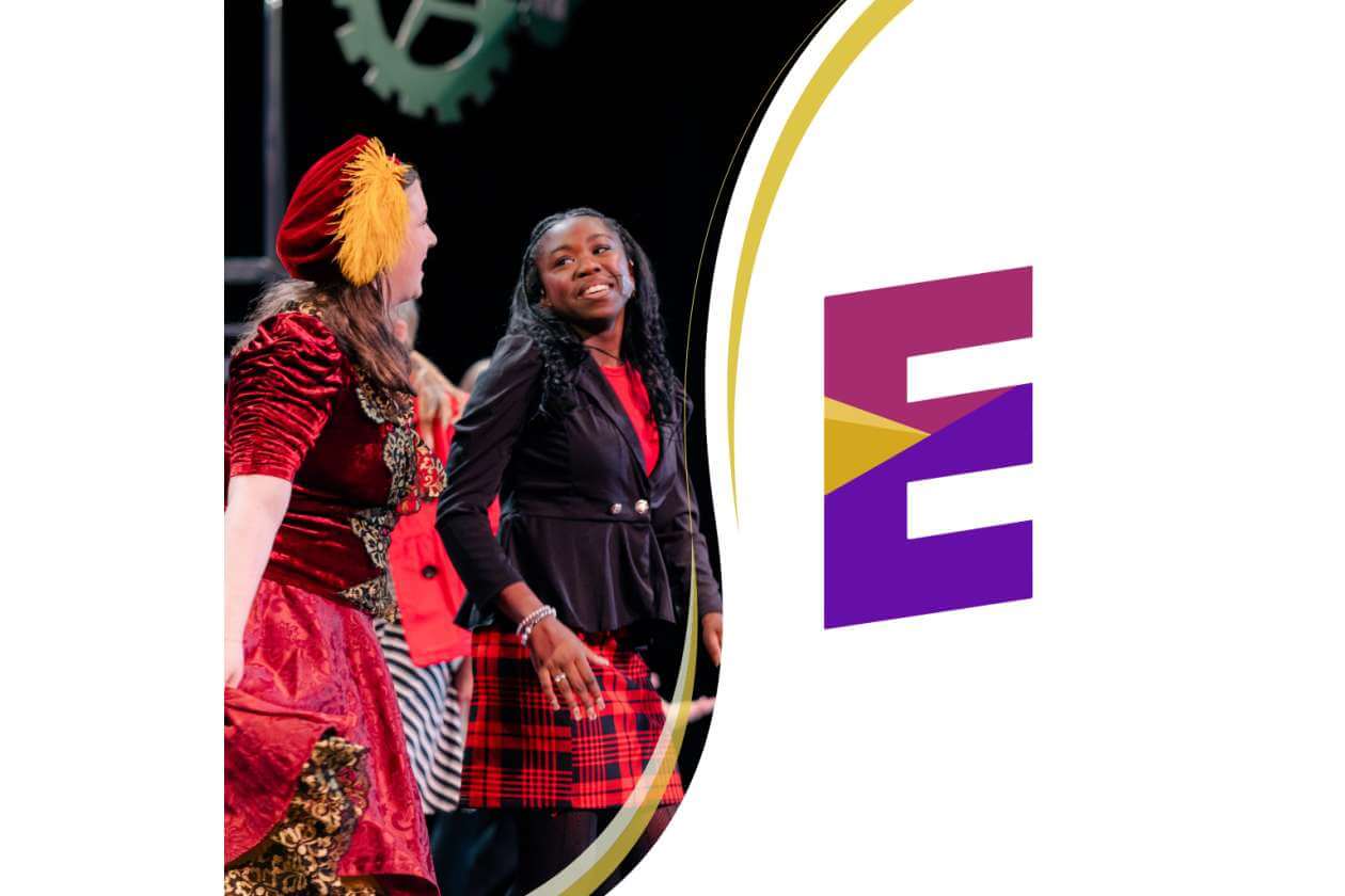 People dancing on stage next to a curved golden arc and a large purple E logo.