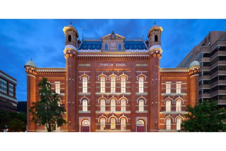 Front facade of Franklin School, a red brick historic building with arched windows, illuminated at dusk.