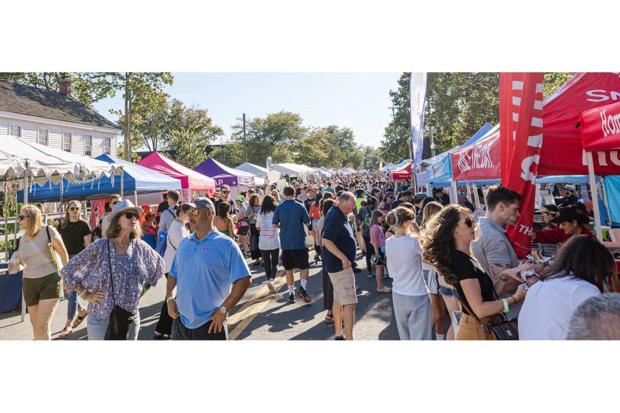 Crowded outdoor street fair with colorful vendor tents and shoppers