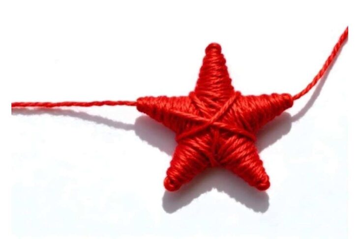Red yarn-wrapped star ornament on a white background, with strings extending from its sides