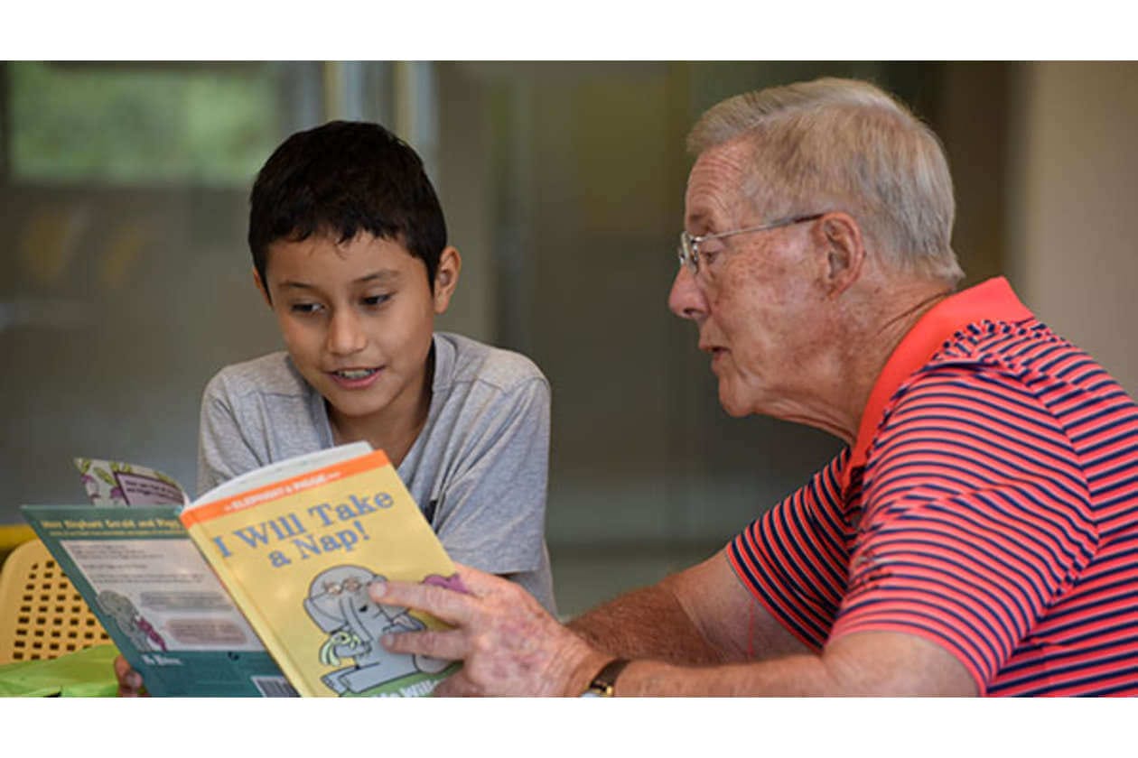 Young boy and an older man reading a colorful children’s book together.