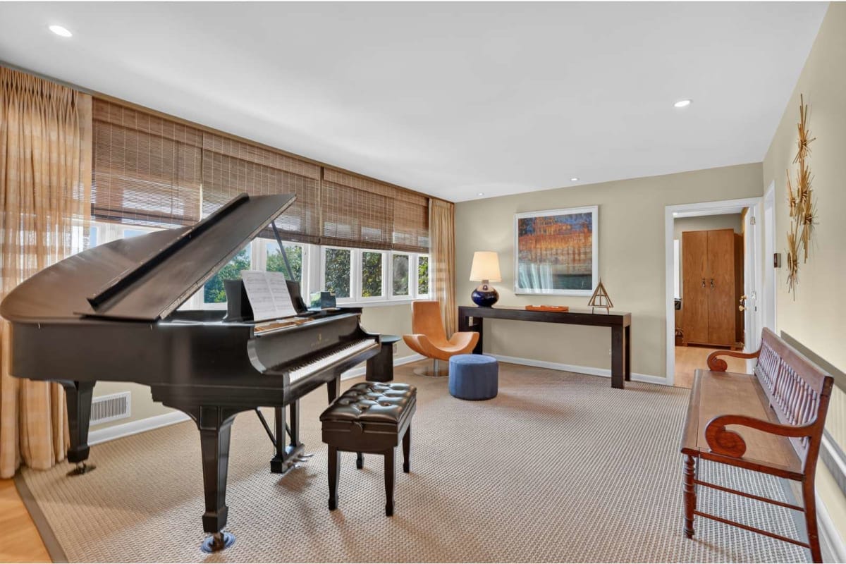 A living room with a black grand piano and matching bench by large windows with wooden blinds.