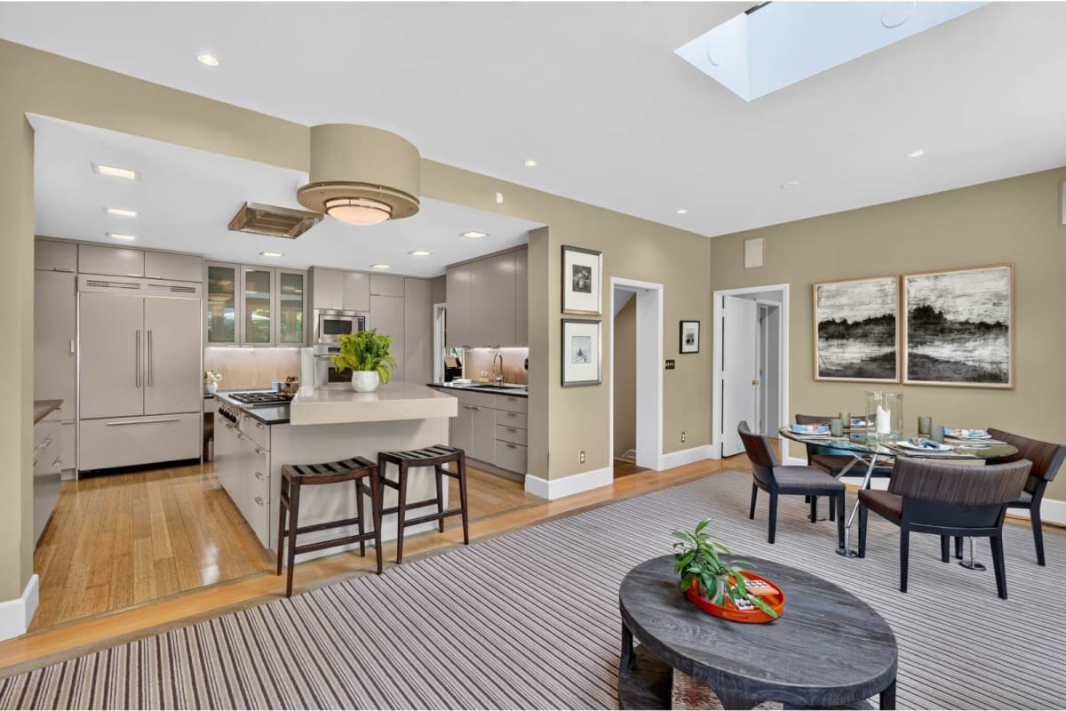 Open-concept kitchen and dining area with an island, gray cabinets, stainless steel appliances, and a striped area rug in warm neutrals.