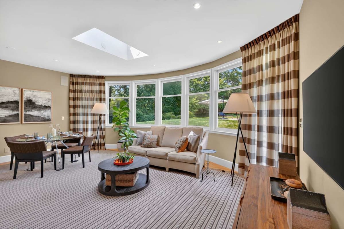 Bright living room with curved bay windows, beige sofa, striped curtains, and a round coffee table.