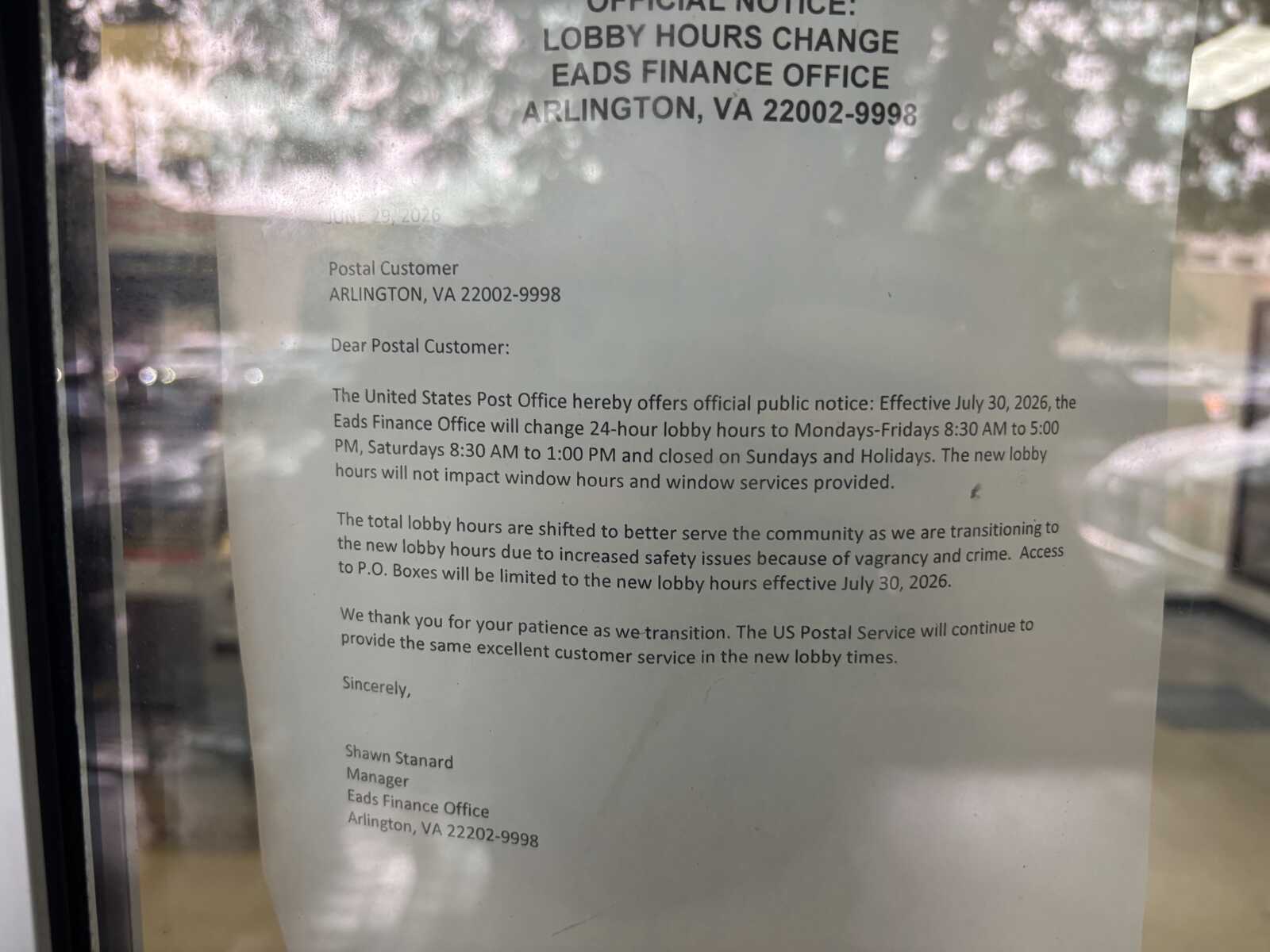 Official notice on glass door about lobby hours change for Arlington, VA post office, effective July 30, 2026.
