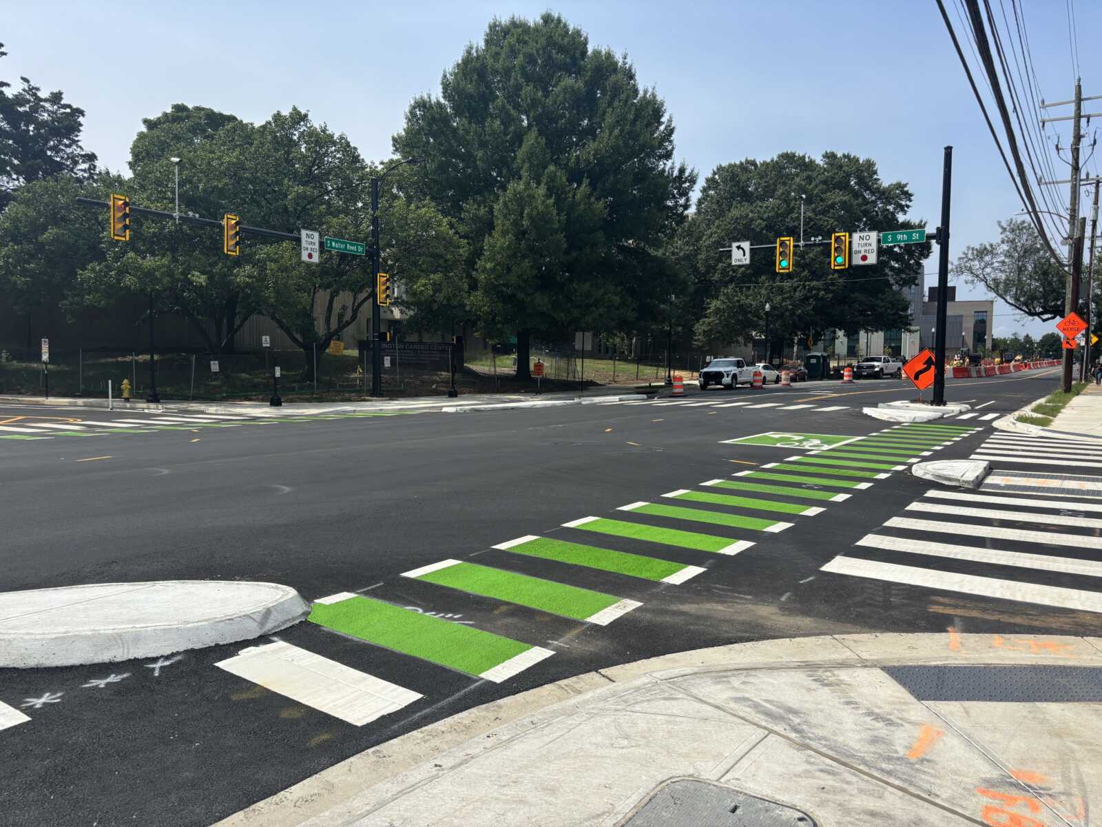 Intersection with bright green bike lanes and white crosswalks, traffic signals, and orange construction cones in the background.