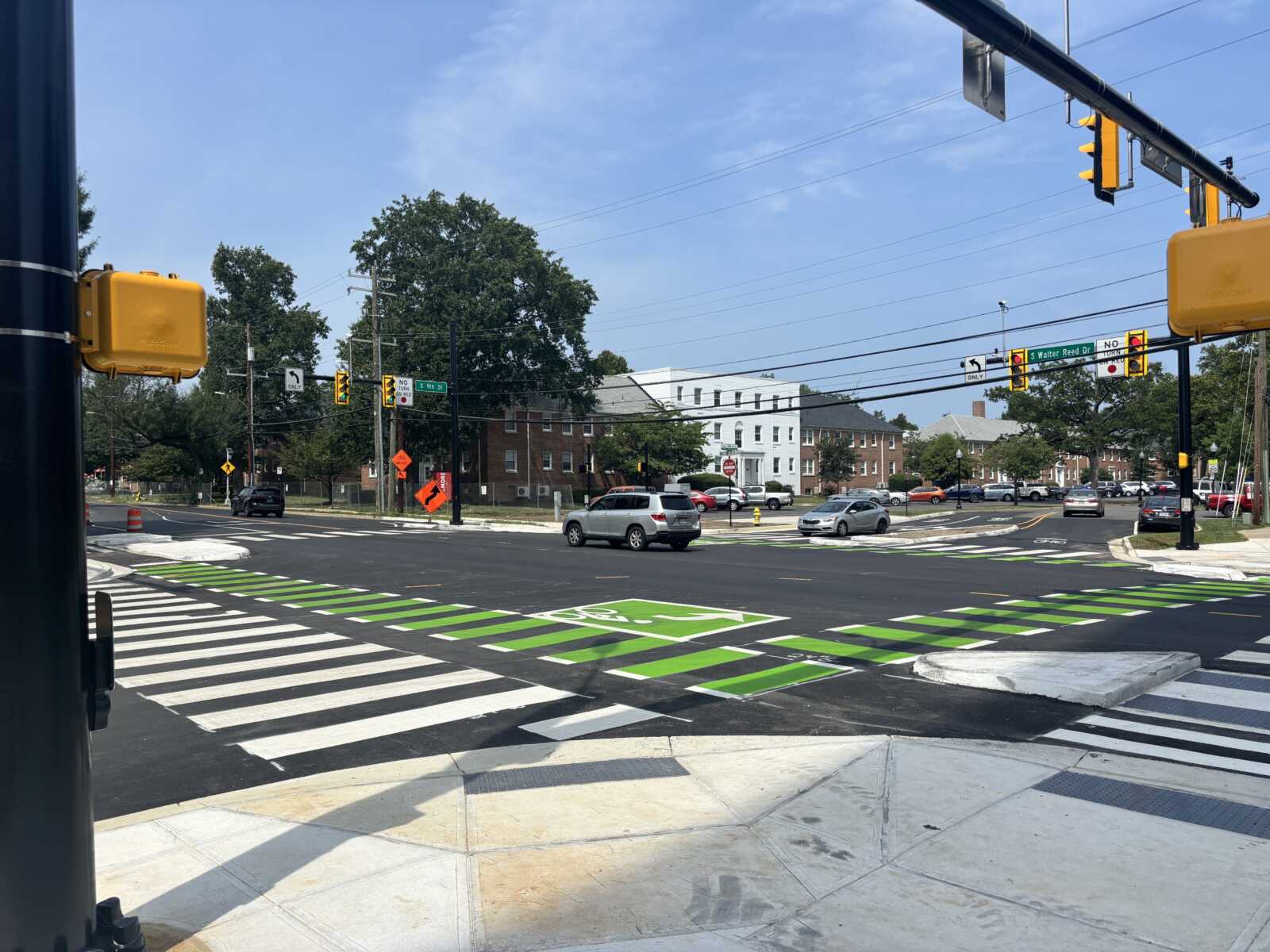 City intersection with bright green bike lanes and wide crosswalks; traffic lights and cars waiting at a sunny day.