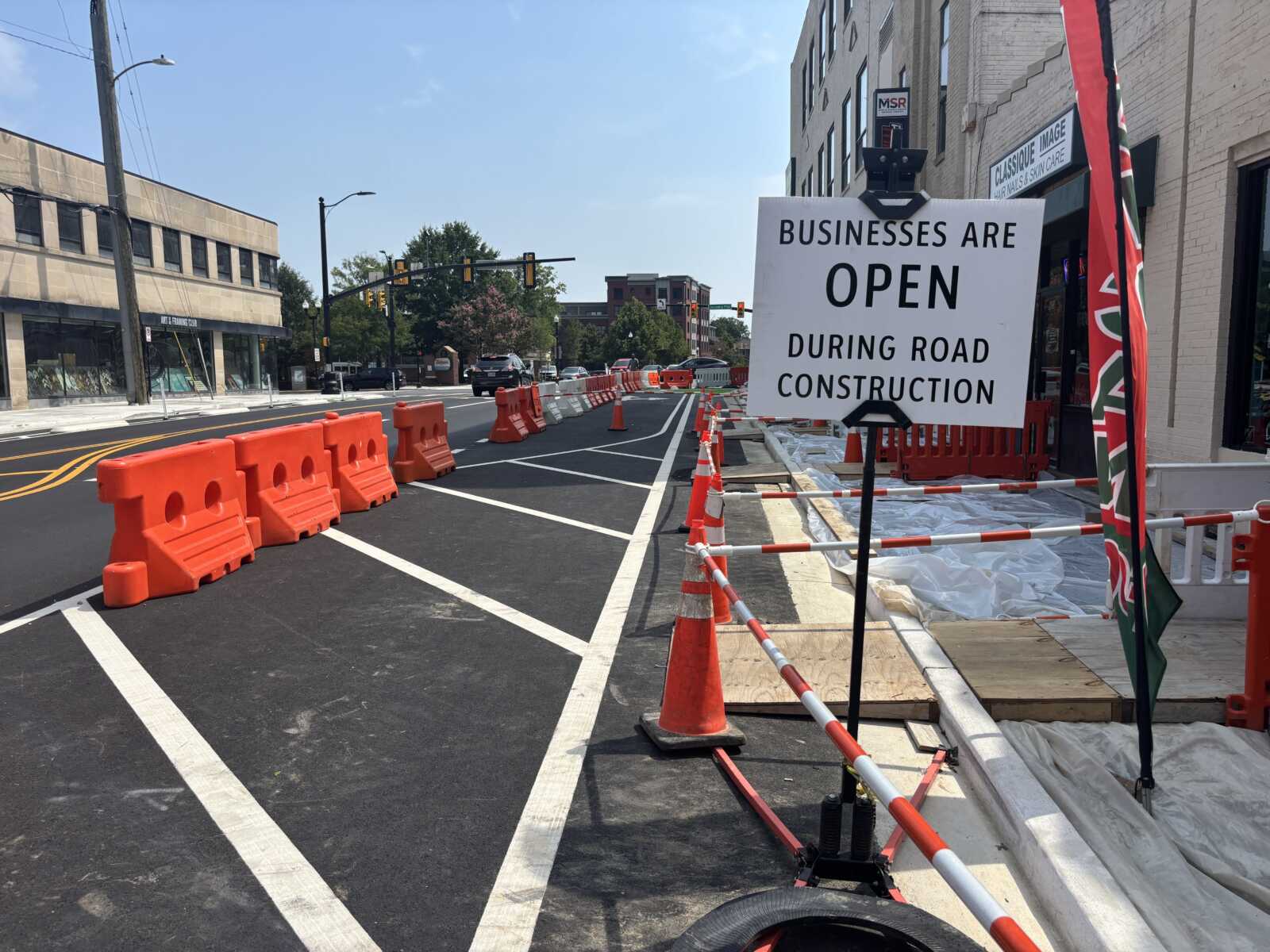 Road construction scene with orange barriers and a sign: 'Businesses are open during road construction' on a busy street.
