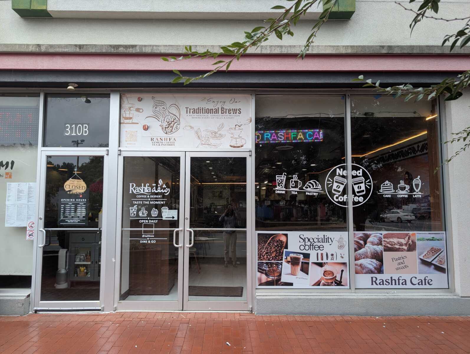 Front of Rashfa Café with glass doors, storefront signs advertising coffee, pastries and desserts, and a brick sidewalk in front.