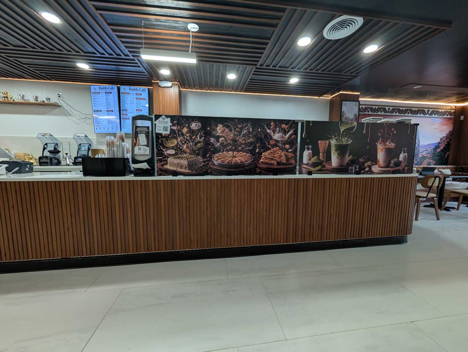 Cafe counter with wooden paneling, pastry displays, and drink machines behind the counter.