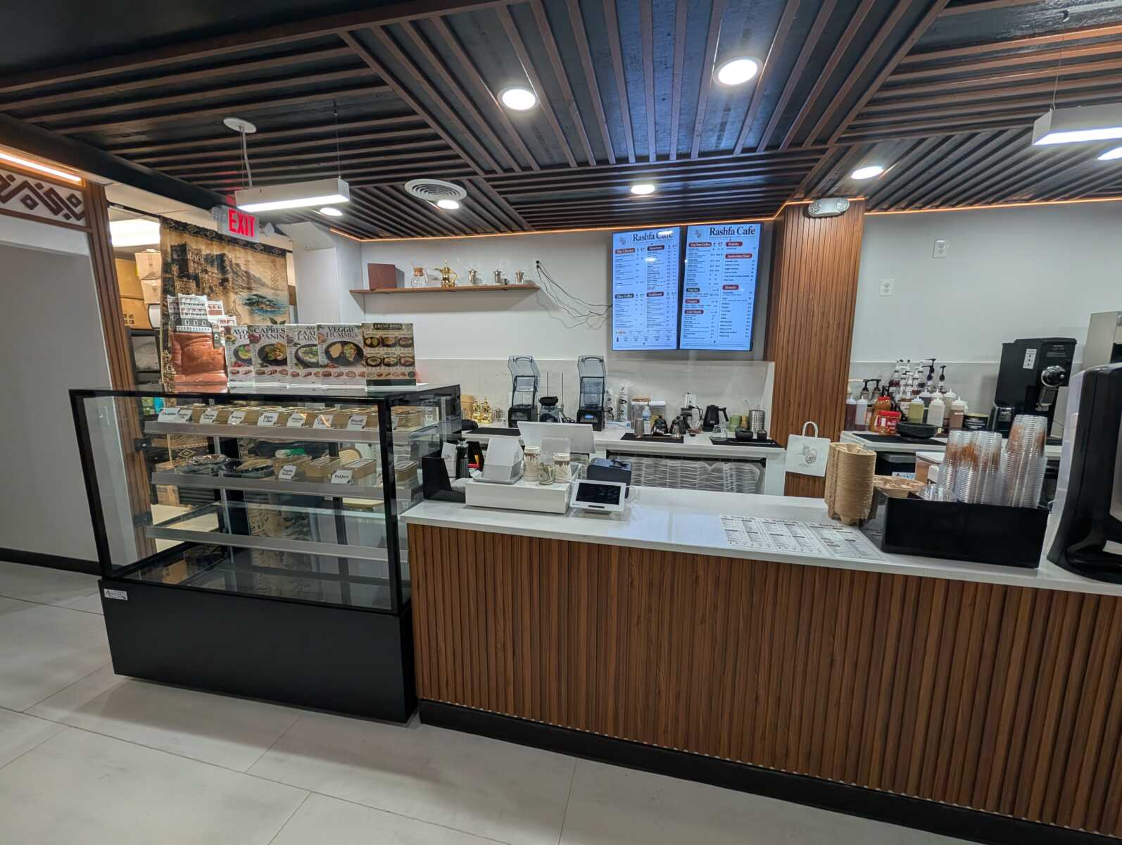Cafe counter inside a modern shop with menu boards, espresso machines, and a glass pastry display.