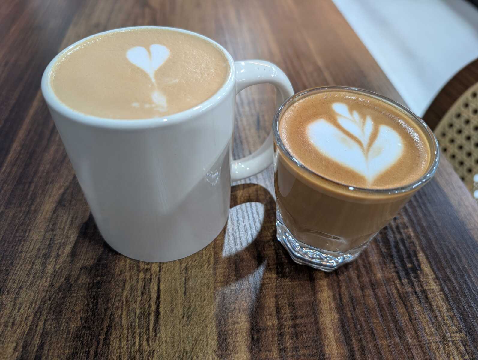 White ceramic mug of latte with a heart-shaped foam art beside a glass of cappuccino on a wooden table