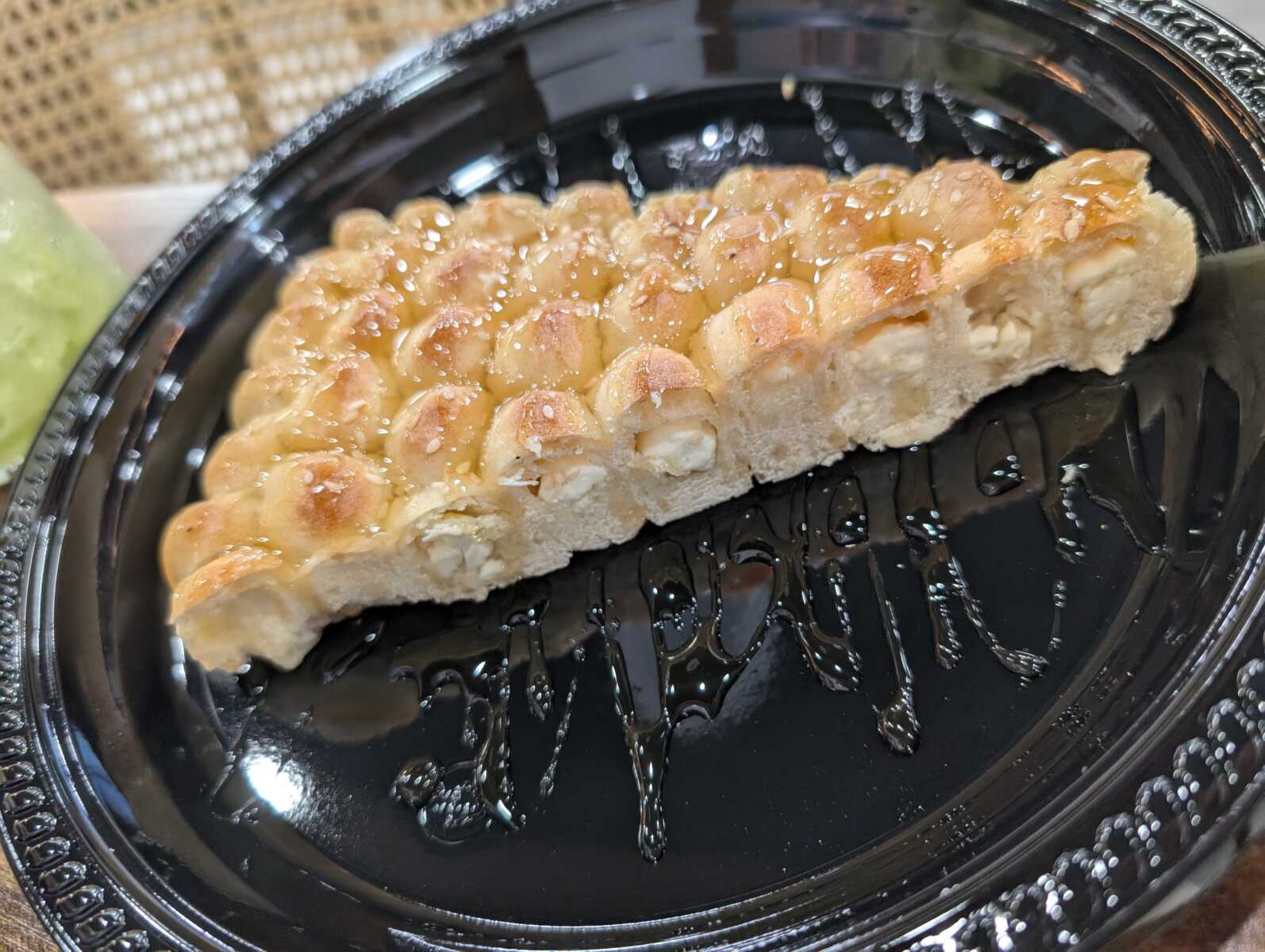 Slice of glazed monkey bread on a black plate with syrup drizzle