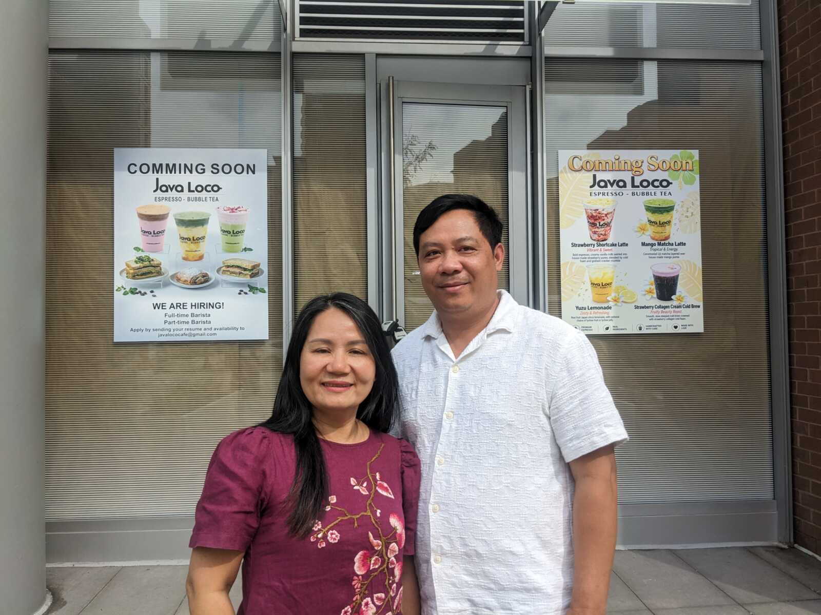 Two people stand in front of a glass storefront with posted