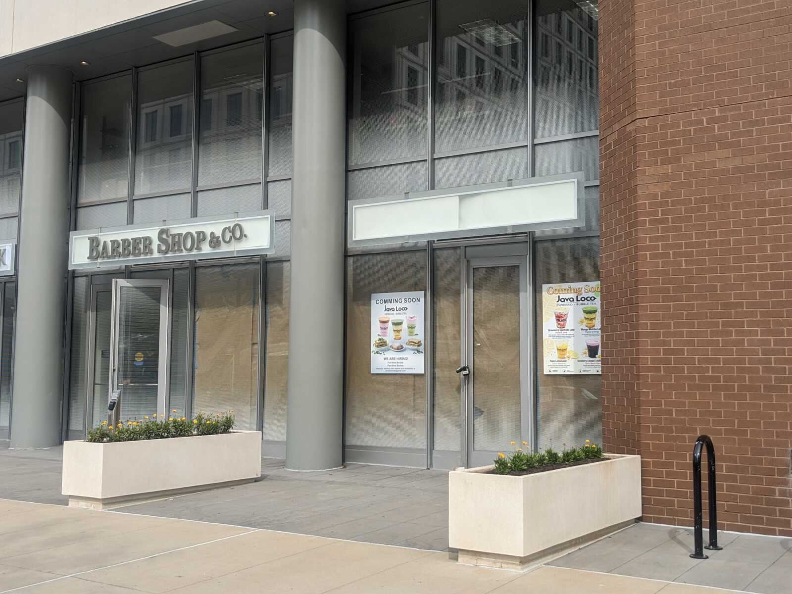 Barber Shop & Co storefront with glass doors, a large sign, and planters with yellow flowers outside the entrance.