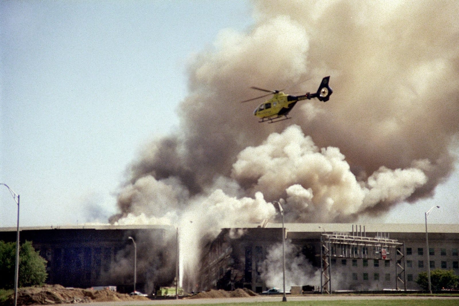 Yellow rescue helicopter hovers above a smoke-filled industrial building as a fire rages below