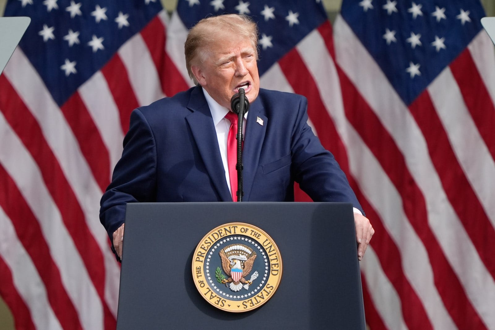 President giving a speech at a podium with the presidential seal, US flags in the background