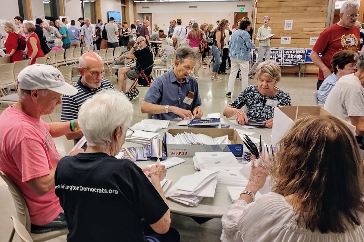 Group of seniors gathered around a table, sorting and filling out papers at a community event in a large hall.