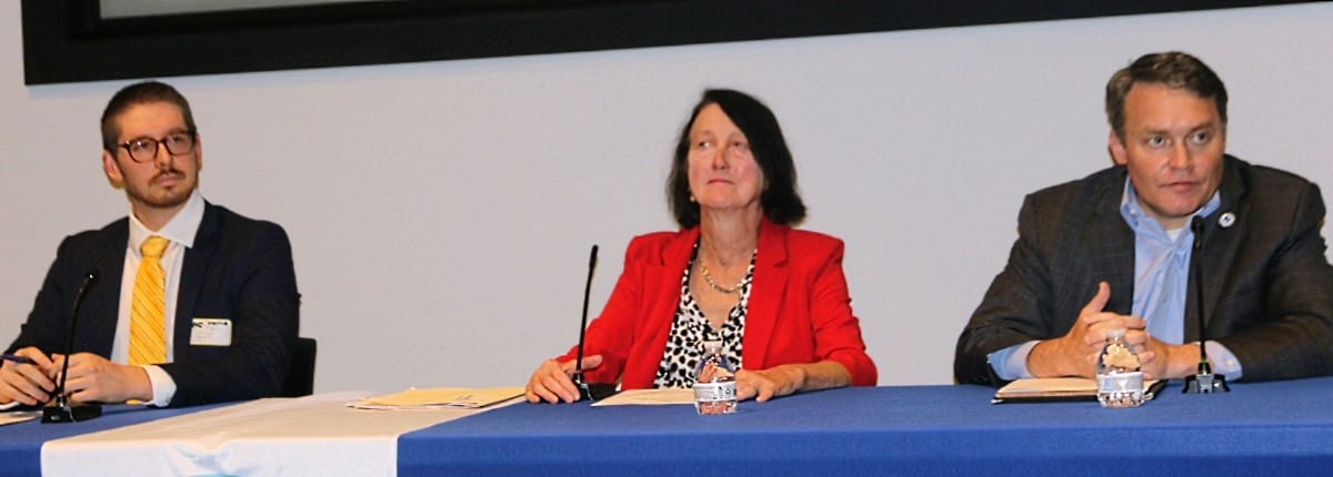 Panelists seated at a long table with blue tablecloth; three people speak into microphones during a discussion.