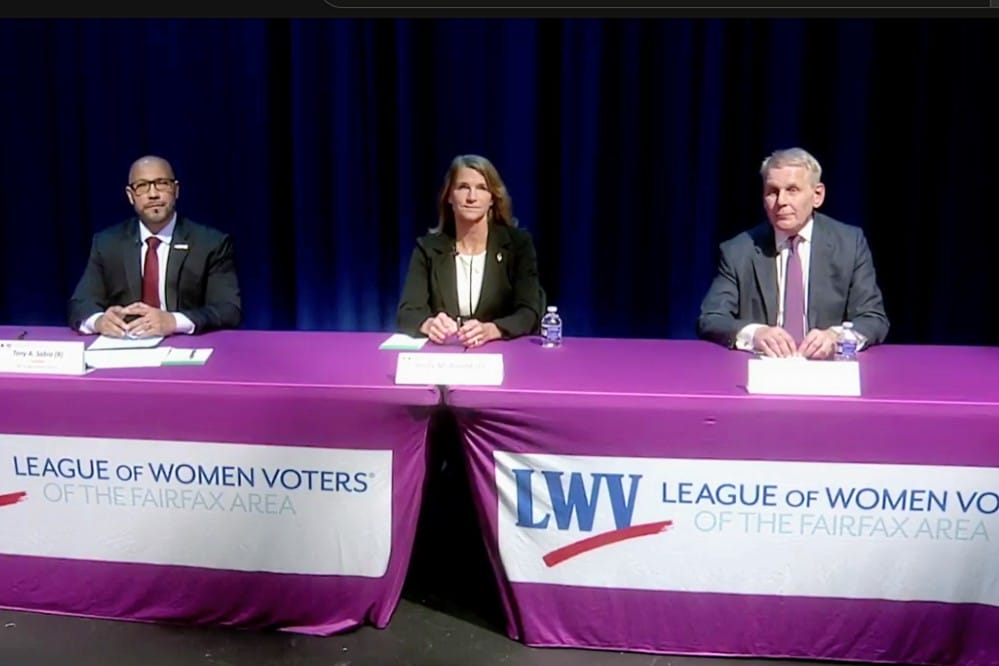 Three panelists sit behind a purple-draped table with League of Women Voters banners at a Fairfax Area event.