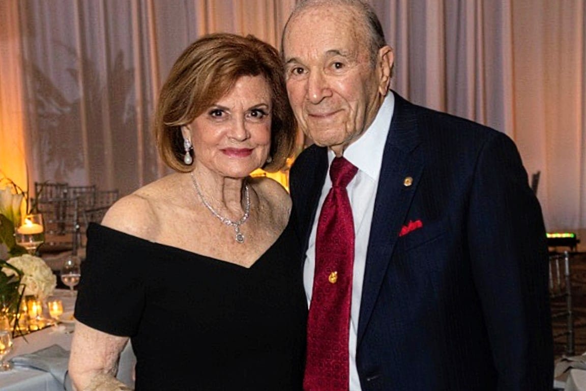 Cynthia and Mort Zetlin (courtesy Arlington Optimist club) | ARLnow An older couple posing together at a formal dinner event, the woman in a black off-the-shoulder dress and jewelry and the man in a dark suit with a red tie.