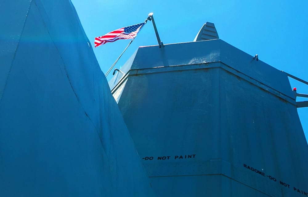 Blue industrial rooftop with an American flag atop a pole, under a clear blue sky; 'DO NOT PAINT' marking on the wall.