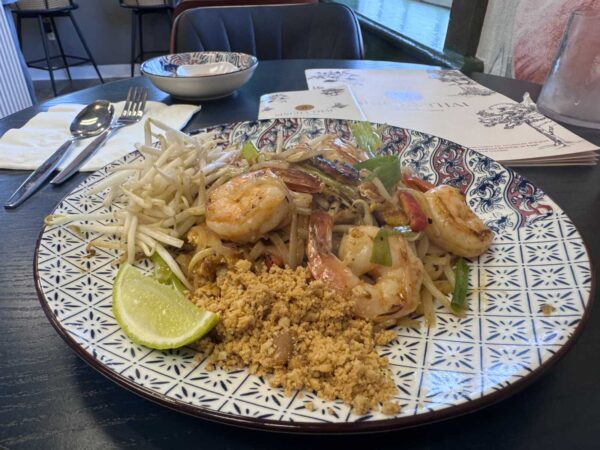 Pad Thai with shrimp, bean sprouts, peanuts, and a lime wedge on a patterned plate at a dining table.