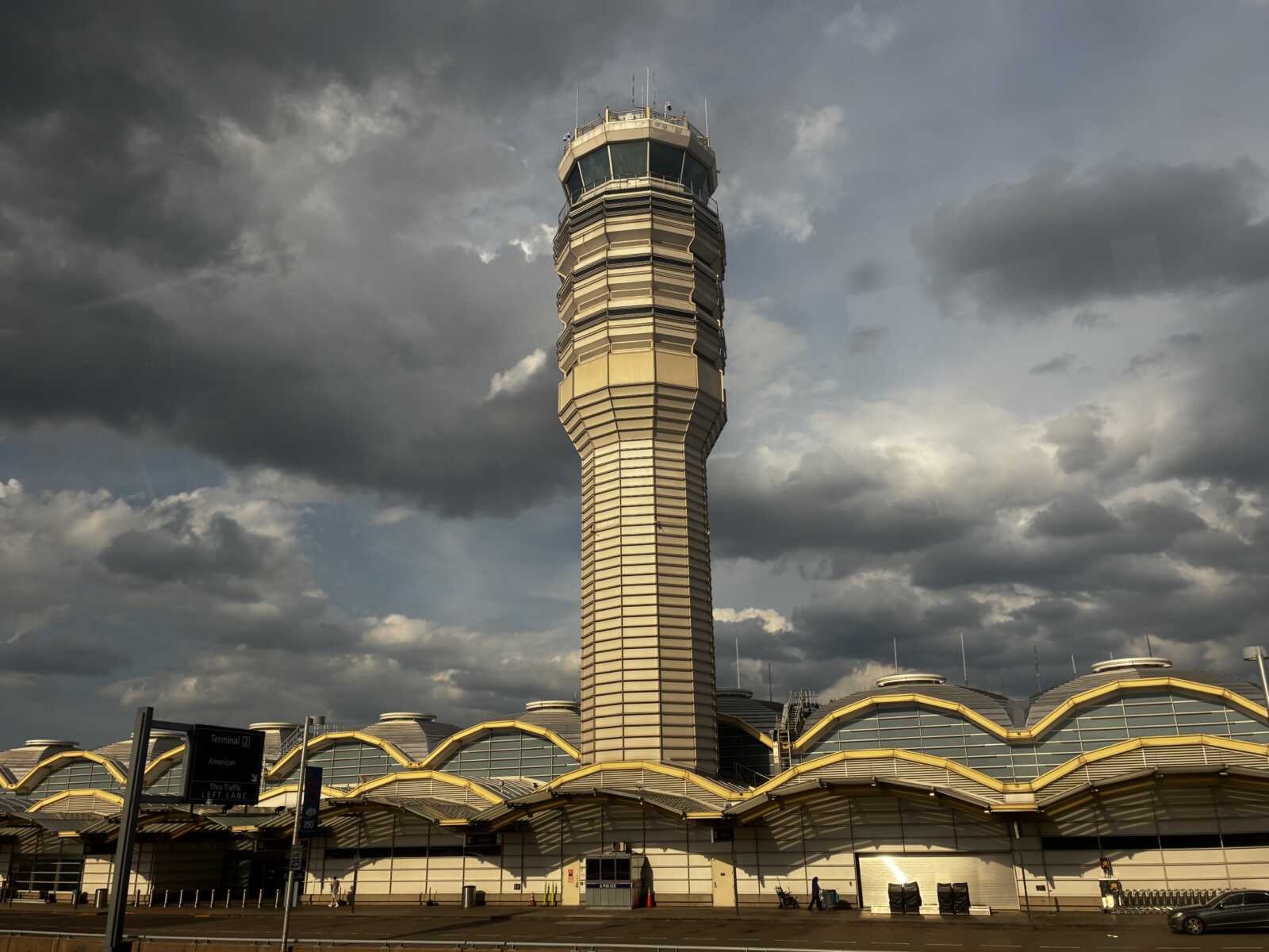 Departures drop-off and the control tower at Reagan National Airport (courtesy George Brazier) | ARLnow Airport control tower rising over a terminal with yellow curved roofs under a cloudy sky a dramatic storm overhead