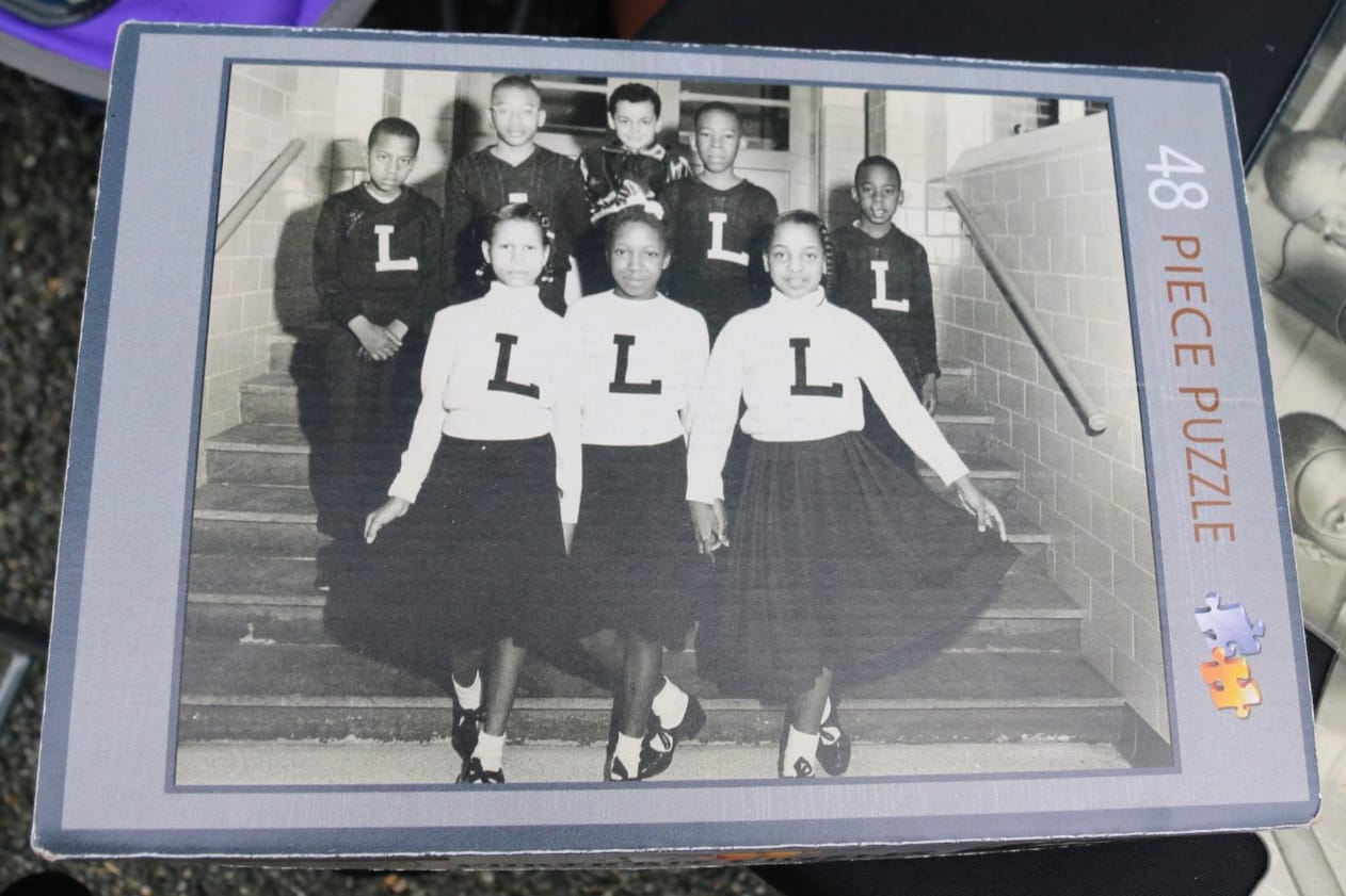 Black-and-white photo of nine girls posing on a stairwell in matching outfits with large'L' on their tops.