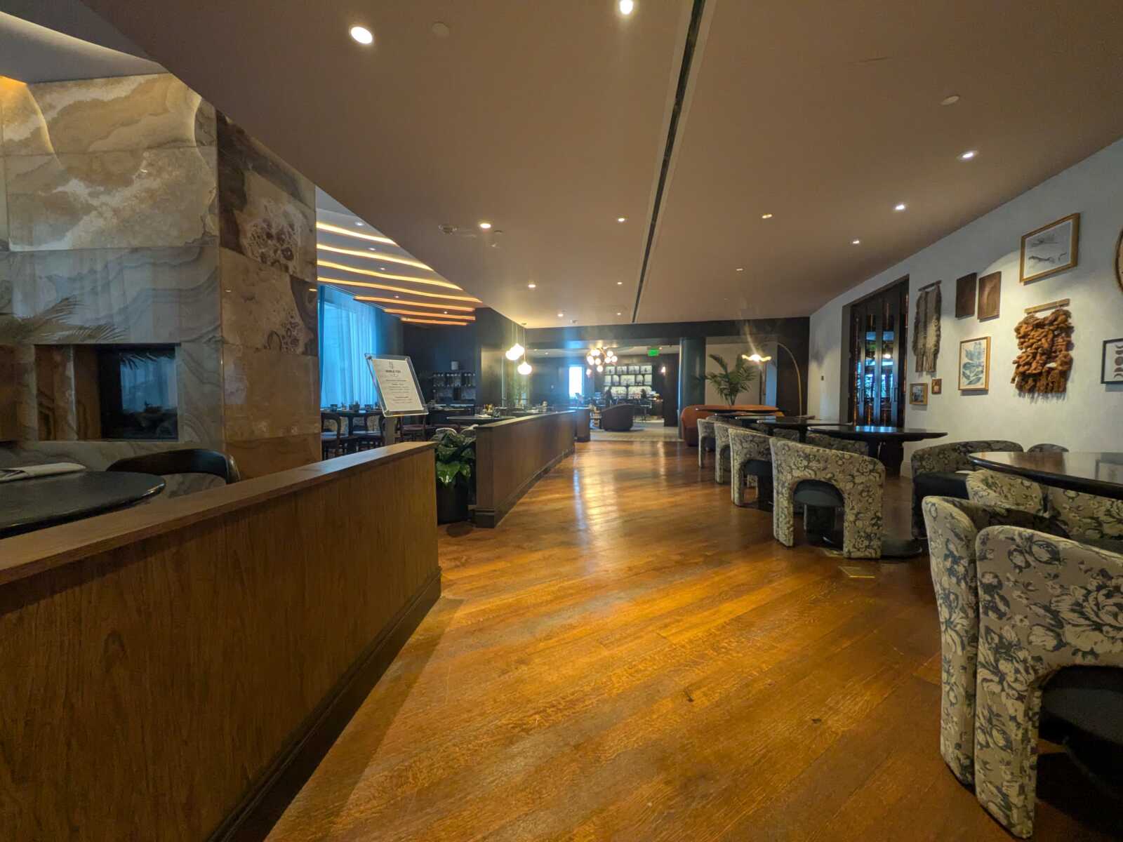 Hotel lobby lounge with a long wood reception desk on the left, patterned chairs along the right, and warm pendant lighting.