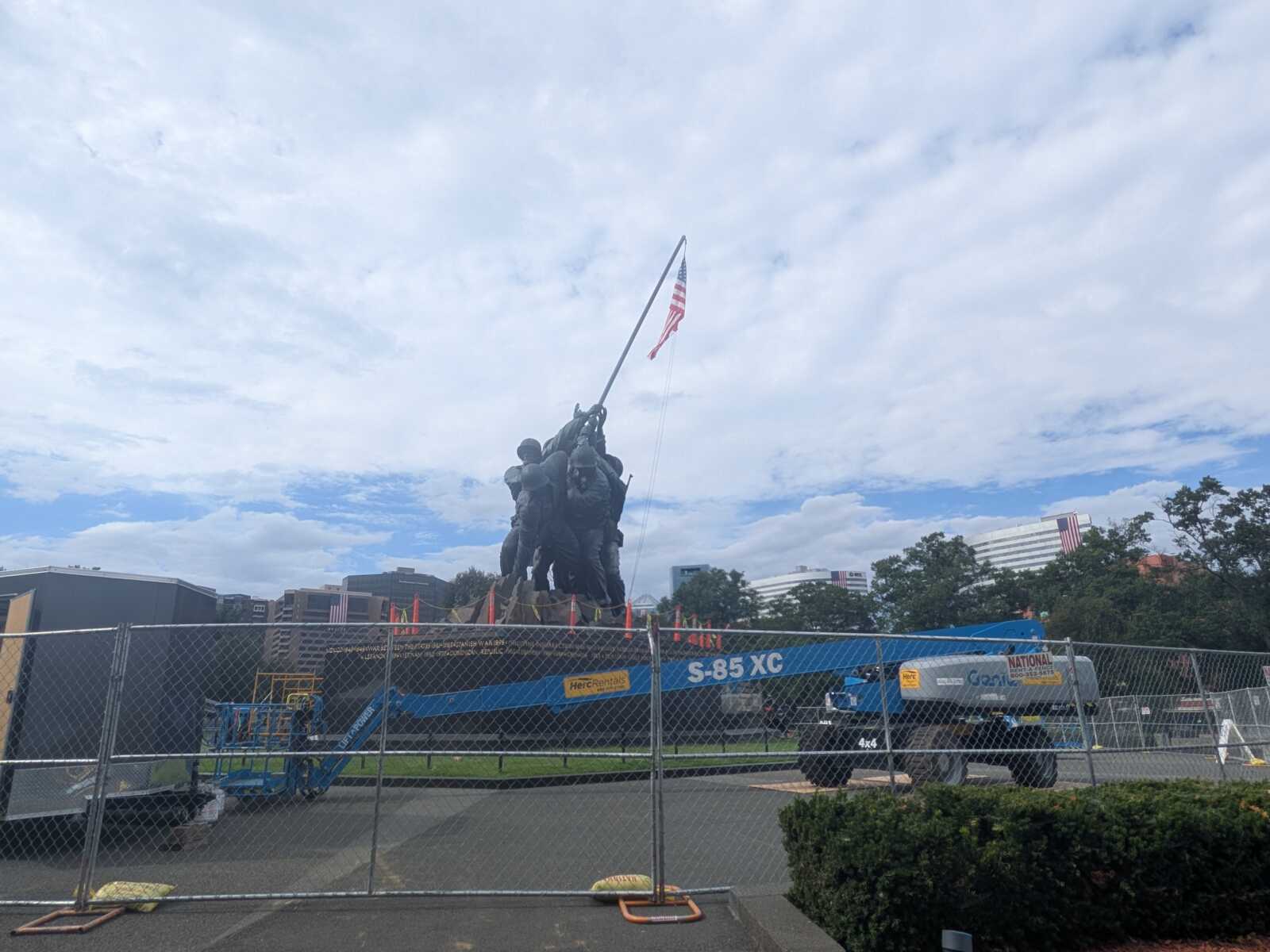 Bronze statue of soldiers raising an American flag, fenced off at a construction site with a tall crane nearby.