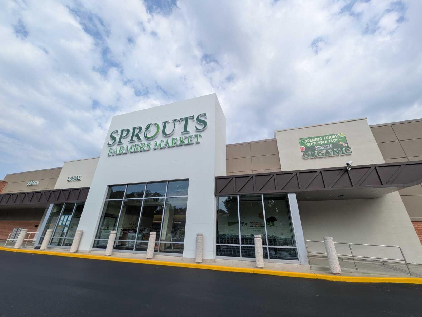 Storefront of Sprouts Farmers Market with a white facade and green signage reading 'SPROUTS FARMERS MARKET' and an 'Organic' banner on the side.