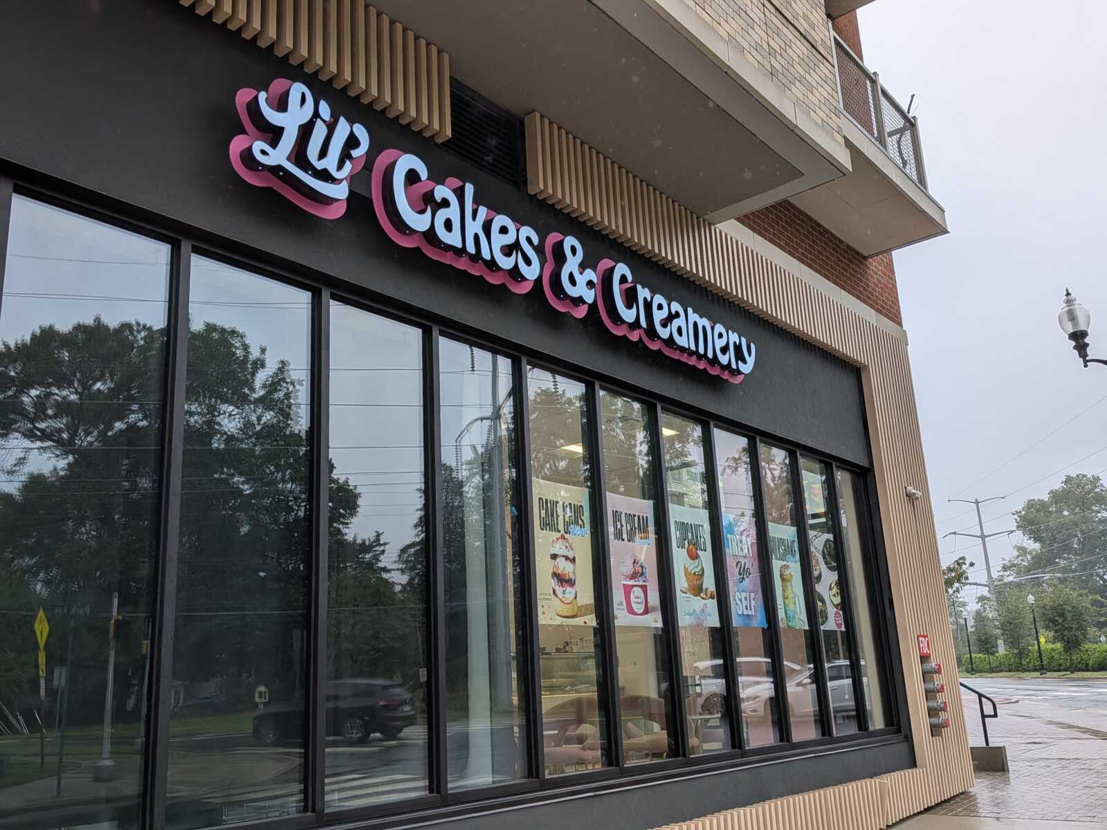 Storefront sign reads 'Lil Cakes & Creamery' with large glass windows and ice cream posters in the display posters in the window.